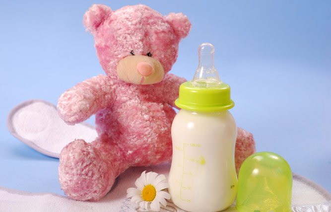 Бутылочка с белой смесью и салатовым колпачком, ромашка и игрушка-медвежонок на голубом фоне
