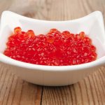 Red caviar in a white plate on a wooden table