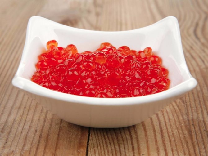 Red caviar in a white plate on a wooden table
