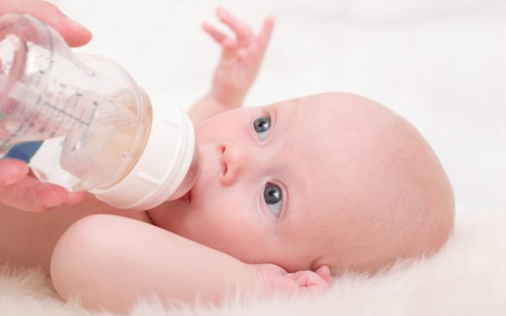 Baby with blue eyes lying down sucking a bottle