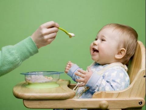 A child in a blue blouse is spoon-fed and laughs