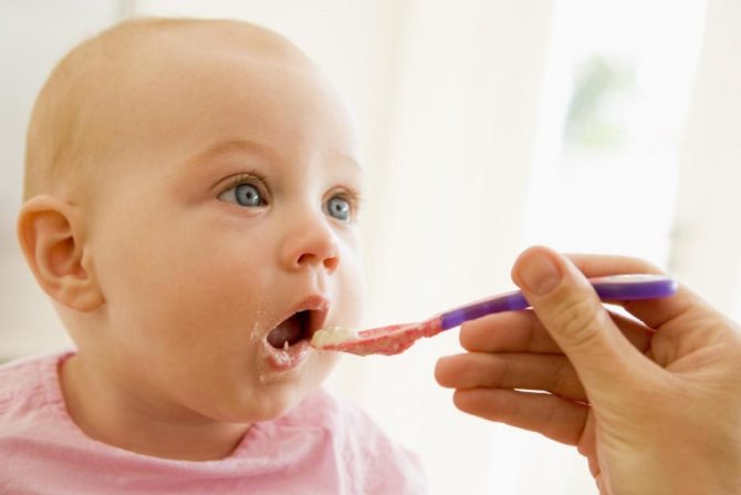 The child opened his mouth and is given complementary foods from a spoon.