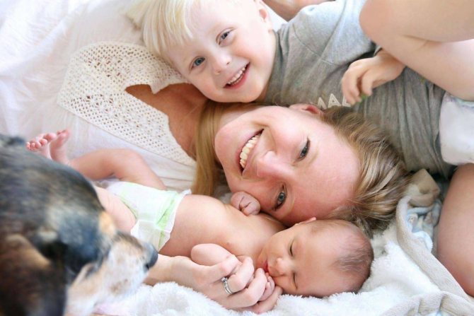 Smiling woman lying with two children and dog on bed