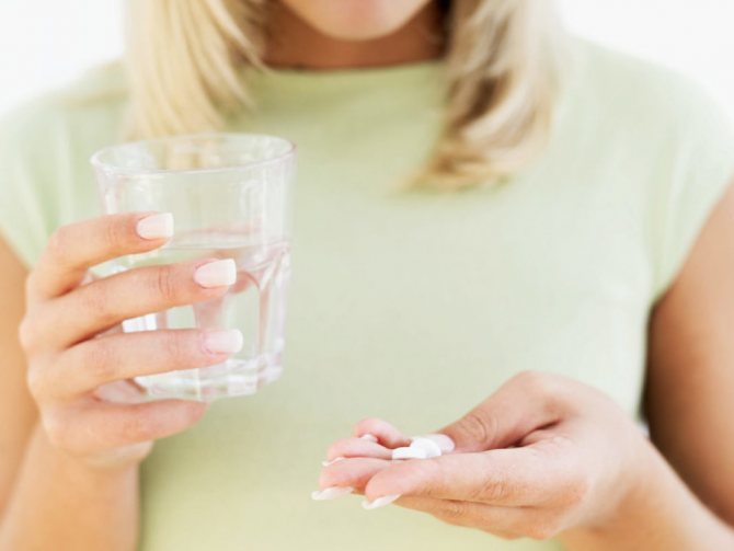 Женщина держит в руках стакан с водой и таблетки