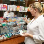 Женщина в белом халате перед витриной с лекарствами